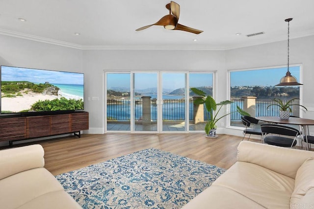 living room with a water view, wood finished floors, a ceiling fan, visible vents, and crown molding