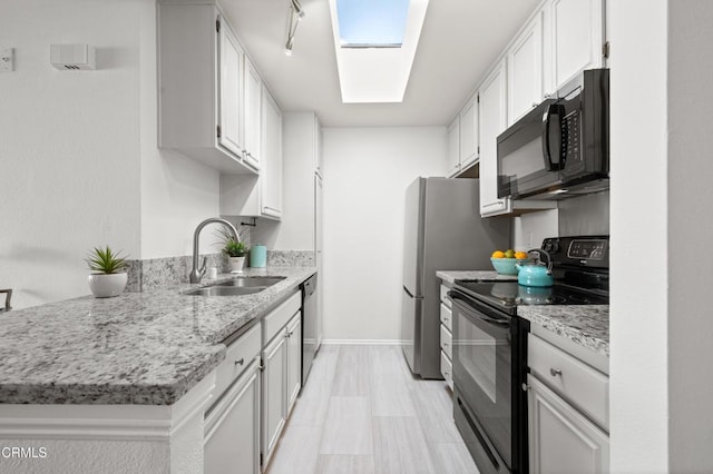 kitchen with a skylight, sink, white cabinets, and black appliances