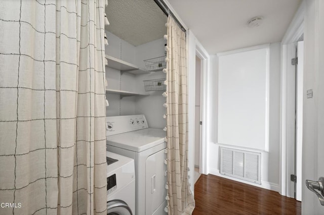 laundry area with a textured ceiling, washing machine and dryer, and dark wood-type flooring