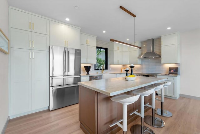 kitchen featuring wall chimney exhaust hood, white cabinetry, appliances with stainless steel finishes, a kitchen island, and pendant lighting