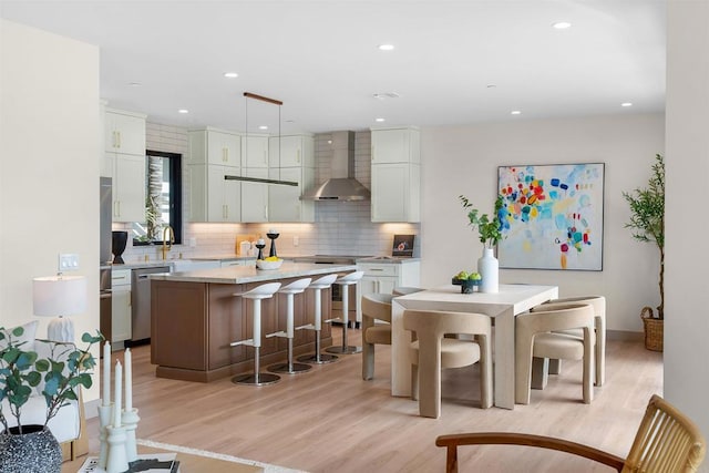 kitchen featuring tasteful backsplash, white cabinetry, hanging light fixtures, a center island, and wall chimney range hood