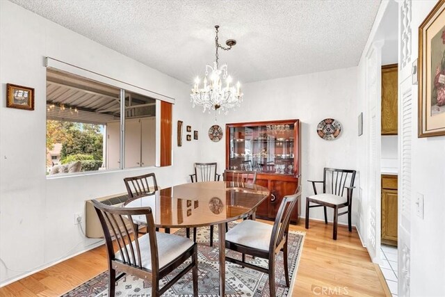 dining area with light hardwood / wood-style flooring, a textured ceiling, and an inviting chandelier