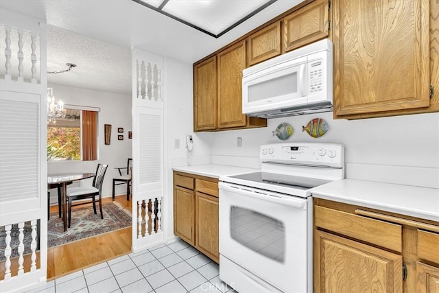 kitchen featuring a textured ceiling, light tile patterned floors, a chandelier, and white appliances