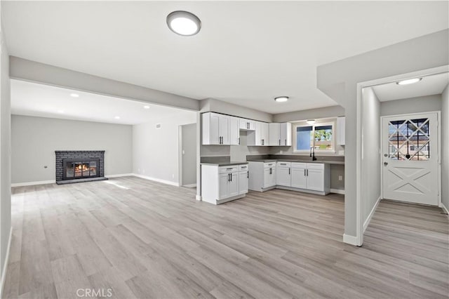 kitchen with white cabinetry, light hardwood / wood-style floors, and a brick fireplace