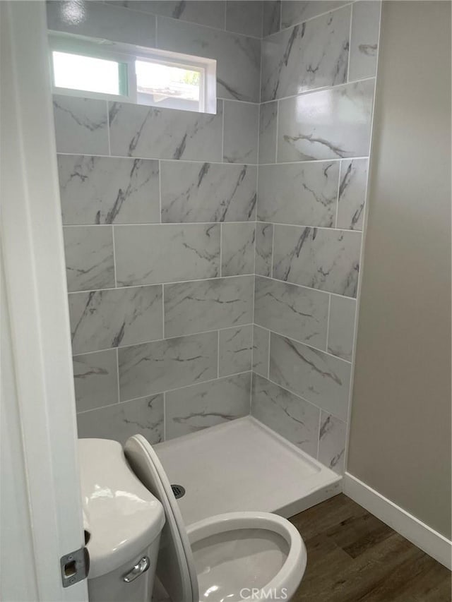 bathroom with tiled shower, hardwood / wood-style floors, and toilet