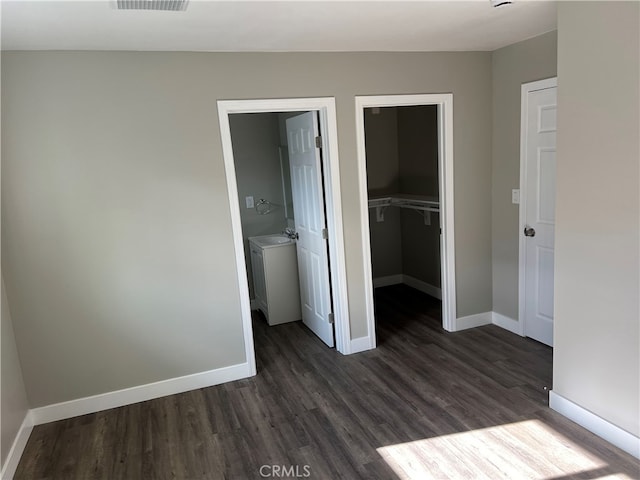 unfurnished bedroom featuring a closet, ensuite bathroom, dark hardwood / wood-style flooring, and a spacious closet