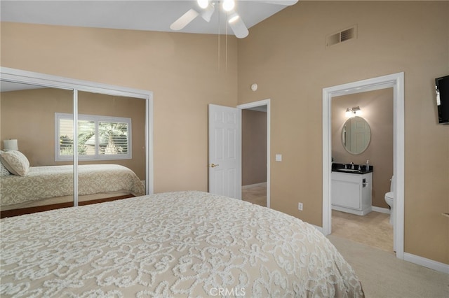 bedroom with ensuite bath, ceiling fan, a closet, and light colored carpet