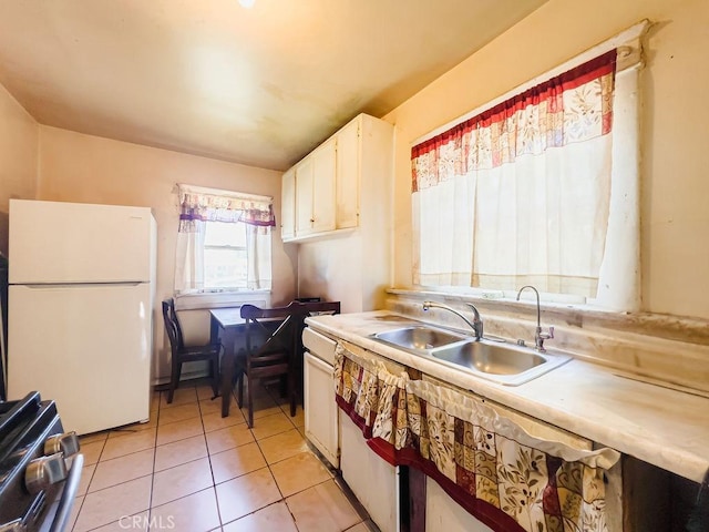 kitchen with sink, black range oven, light tile patterned floors, white fridge, and white cabinets