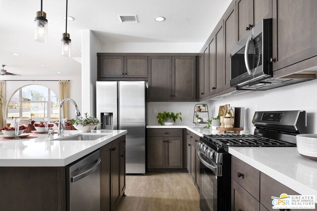 kitchen featuring pendant lighting, sink, light hardwood / wood-style flooring, dark brown cabinets, and stainless steel appliances