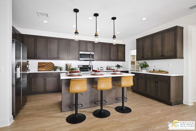 kitchen with dark brown cabinetry, hanging light fixtures, stainless steel appliances, light hardwood / wood-style floors, and a kitchen island