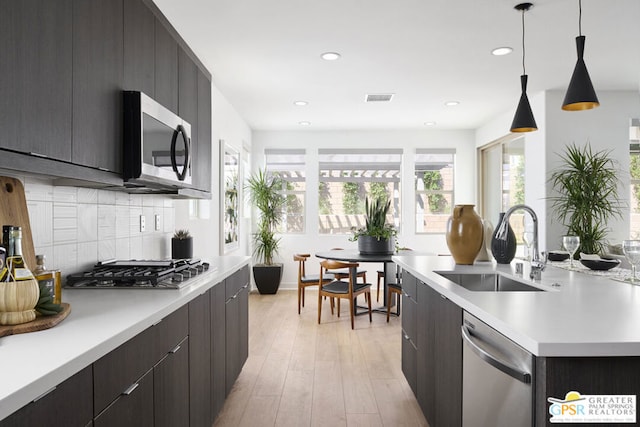 kitchen featuring sink, hanging light fixtures, tasteful backsplash, light hardwood / wood-style floors, and appliances with stainless steel finishes