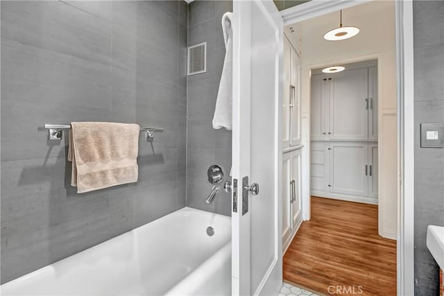 bathroom with hardwood / wood-style floors and tiled shower / bath