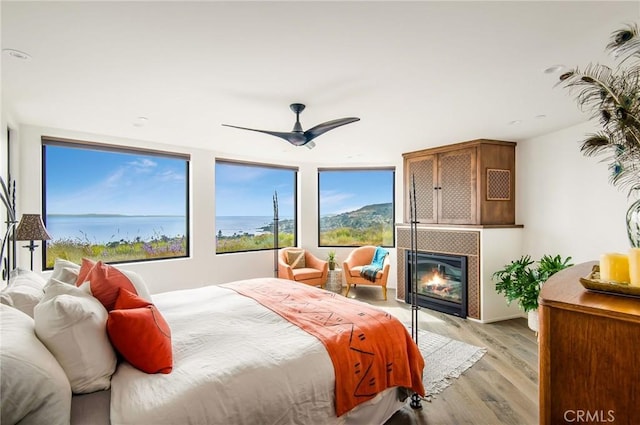 bedroom featuring light wood-style flooring, a tile fireplace, and ceiling fan