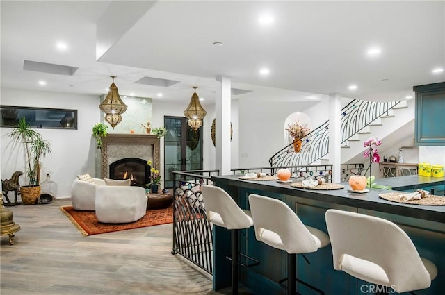 bar featuring stairs, wood finished floors, a glass covered fireplace, and recessed lighting