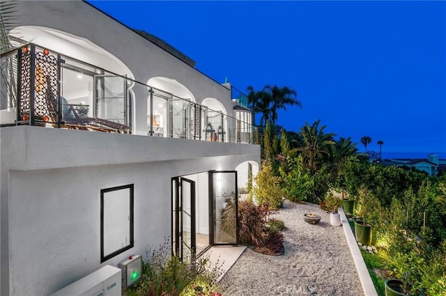 property exterior at night with a balcony and stucco siding