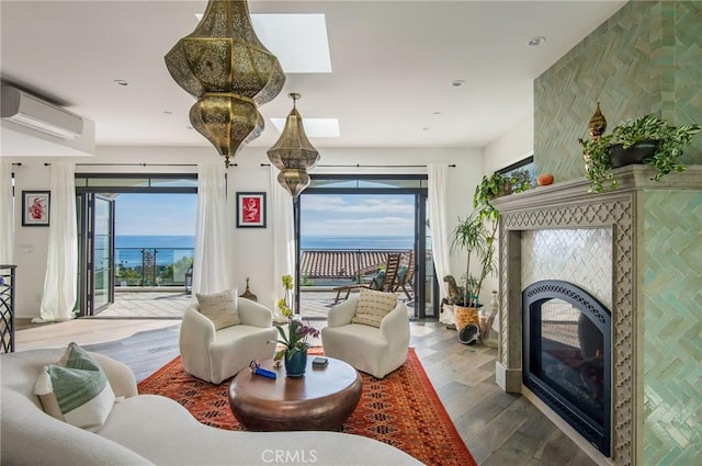 interior space with a wall mounted air conditioner, a water view, a skylight, hardwood / wood-style flooring, and a large fireplace