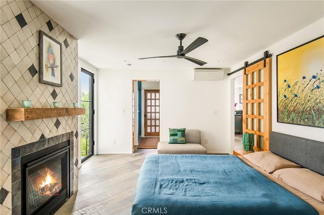 interior space featuring a wall mounted air conditioner, light wood-type flooring, a tile fireplace, and ceiling fan