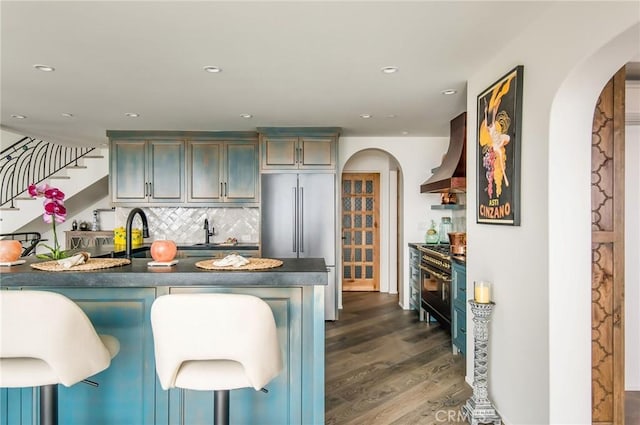 kitchen with a breakfast bar, premium range hood, decorative backsplash, premium appliances, and dark hardwood / wood-style flooring