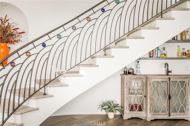 staircase with indoor wet bar and wood finished floors
