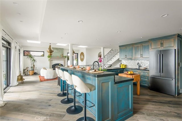 kitchen featuring high end fridge, a breakfast bar area, wood finished floors, a large fireplace, and dark countertops