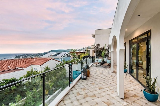 balcony at dusk featuring a water view