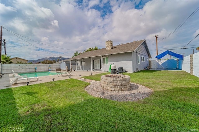 back of property featuring a patio, a lawn, an outdoor fire pit, a shed, and a fenced in pool