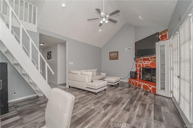 living room featuring high vaulted ceiling, a wealth of natural light, a stone fireplace, and hardwood / wood-style flooring