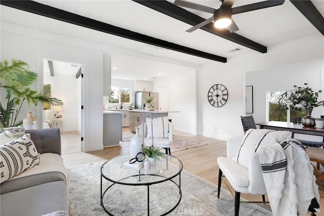 living room with ceiling fan, beamed ceiling, and light hardwood / wood-style floors