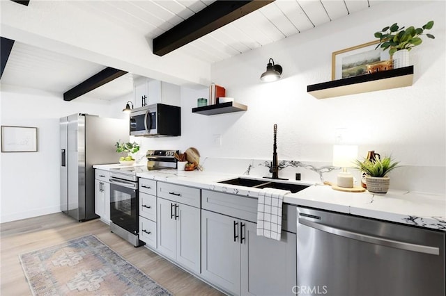 kitchen featuring beamed ceiling, light wood-type flooring, sink, and appliances with stainless steel finishes