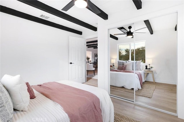 bedroom featuring beam ceiling, light wood-type flooring, a closet, and ceiling fan