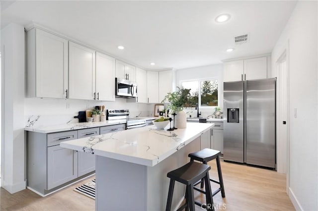 kitchen featuring light stone counters, light hardwood / wood-style flooring, a breakfast bar area, a kitchen island, and appliances with stainless steel finishes