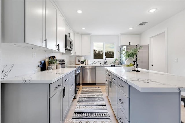 kitchen with a center island, sink, light hardwood / wood-style flooring, light stone countertops, and stainless steel appliances