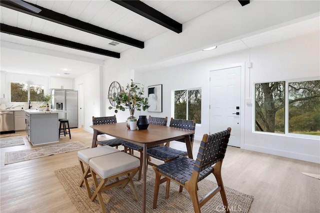 dining space with beamed ceiling, light hardwood / wood-style floors, and a healthy amount of sunlight