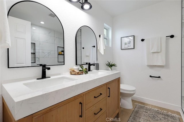 bathroom featuring hardwood / wood-style floors, vanity, toilet, and a tile shower