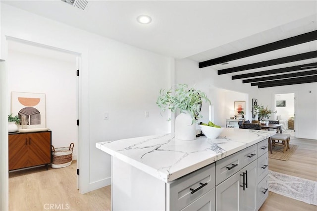 kitchen featuring beam ceiling, light stone countertops, a kitchen island, and light hardwood / wood-style floors