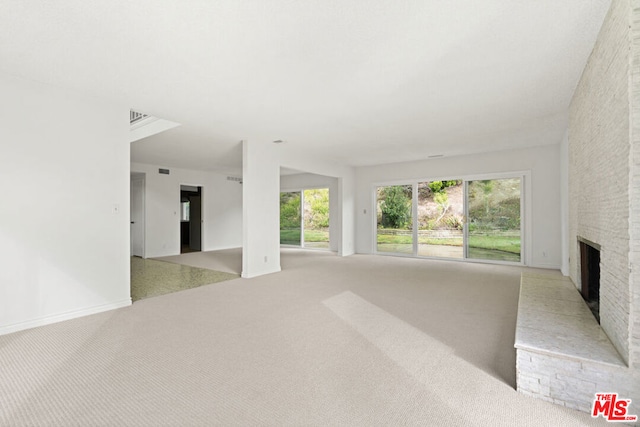 unfurnished living room featuring light colored carpet and a brick fireplace