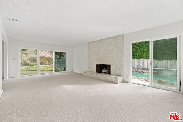 unfurnished living room featuring light carpet, a textured ceiling, and a stone fireplace