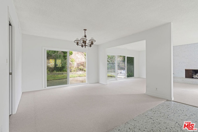 unfurnished living room featuring a fireplace, light colored carpet, a textured ceiling, and an inviting chandelier