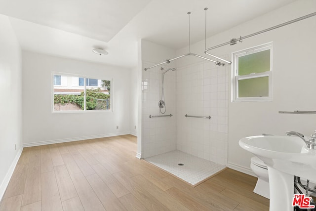 bathroom with toilet, hardwood / wood-style floors, and tiled shower