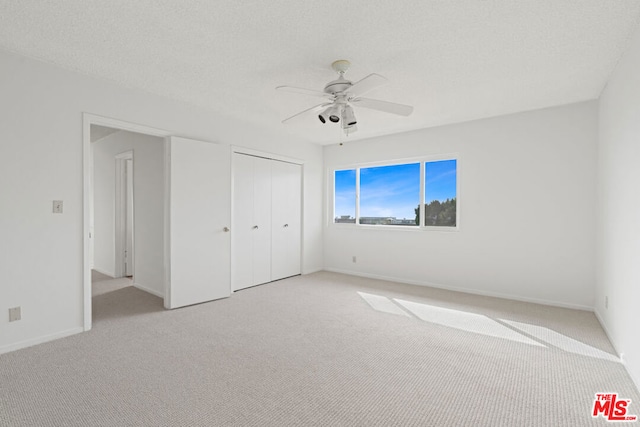 unfurnished bedroom with ceiling fan, light colored carpet, a textured ceiling, and a closet