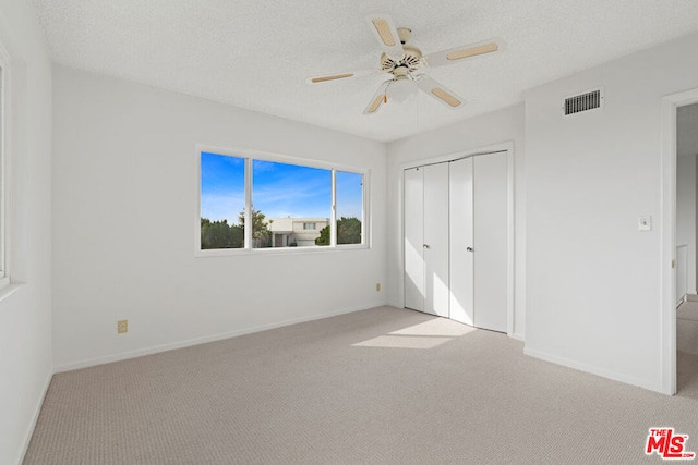 unfurnished bedroom featuring ceiling fan, a textured ceiling, light carpet, and a closet