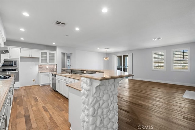 kitchen with white cabinets, wood-type flooring, an island with sink, and appliances with stainless steel finishes