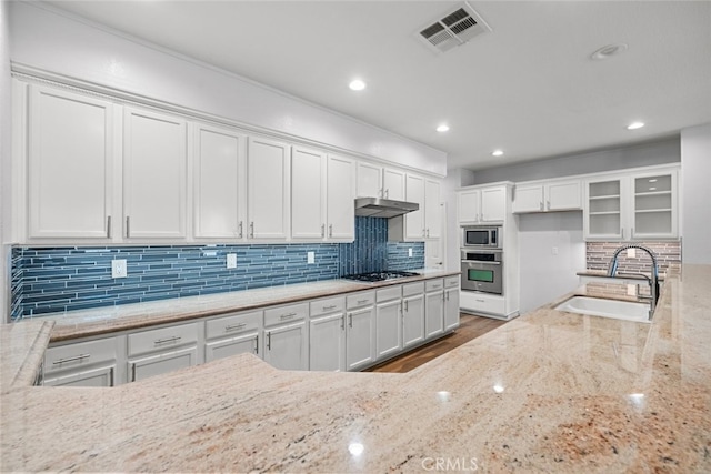 kitchen with light stone countertops, sink, stainless steel appliances, backsplash, and white cabinets