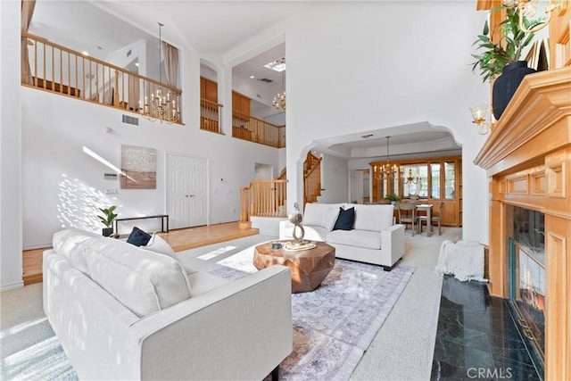 carpeted living room featuring a towering ceiling, an inviting chandelier, and a premium fireplace