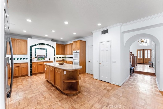 kitchen featuring white double oven, a center island with sink, crown molding, decorative backsplash, and stainless steel refrigerator