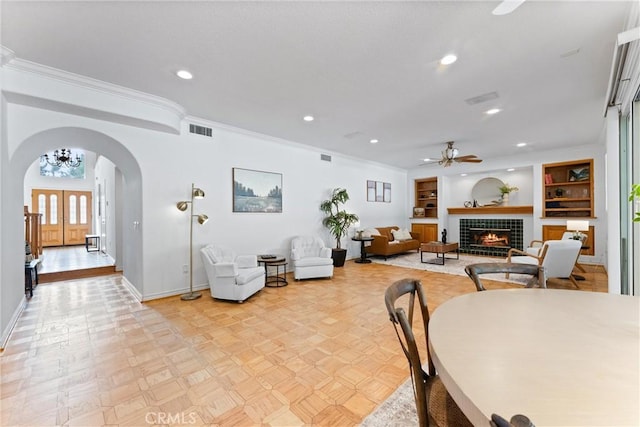 dining area with ceiling fan, built in features, light parquet floors, a fireplace, and ornamental molding