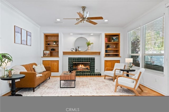 sitting room with ceiling fan, built in features, ornamental molding, a fireplace, and light wood-type flooring