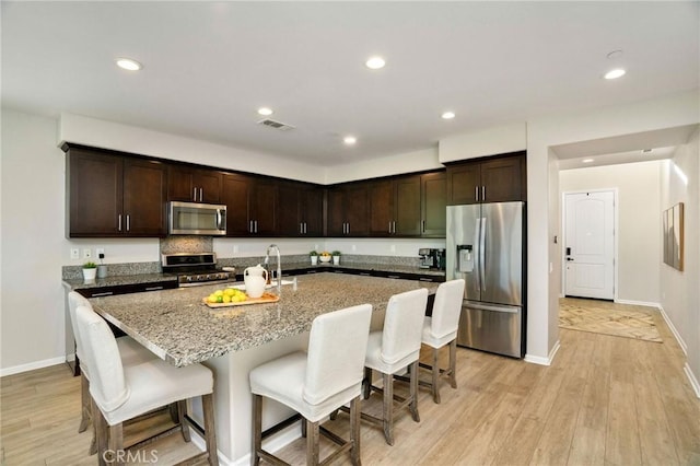 kitchen featuring dark brown cabinetry, light stone countertops, light hardwood / wood-style floors, a breakfast bar area, and appliances with stainless steel finishes