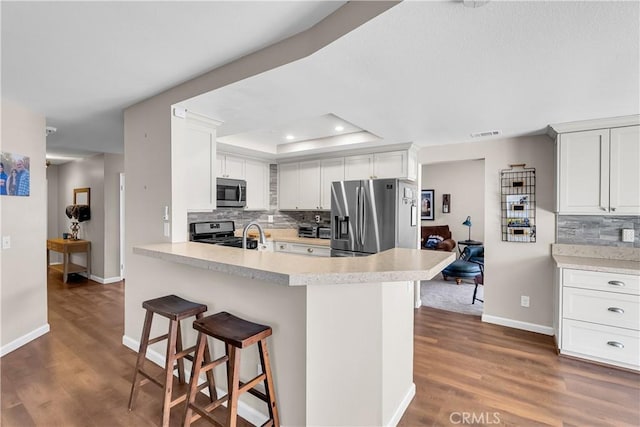 kitchen featuring a breakfast bar, appliances with stainless steel finishes, a tray ceiling, and white cabinetry