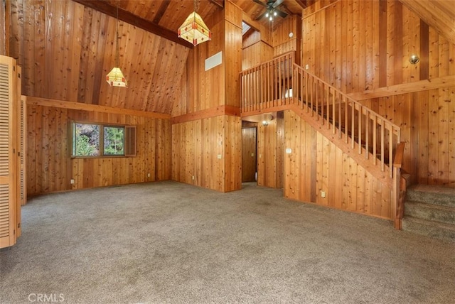 unfurnished living room featuring carpet floors, high vaulted ceiling, and wooden walls